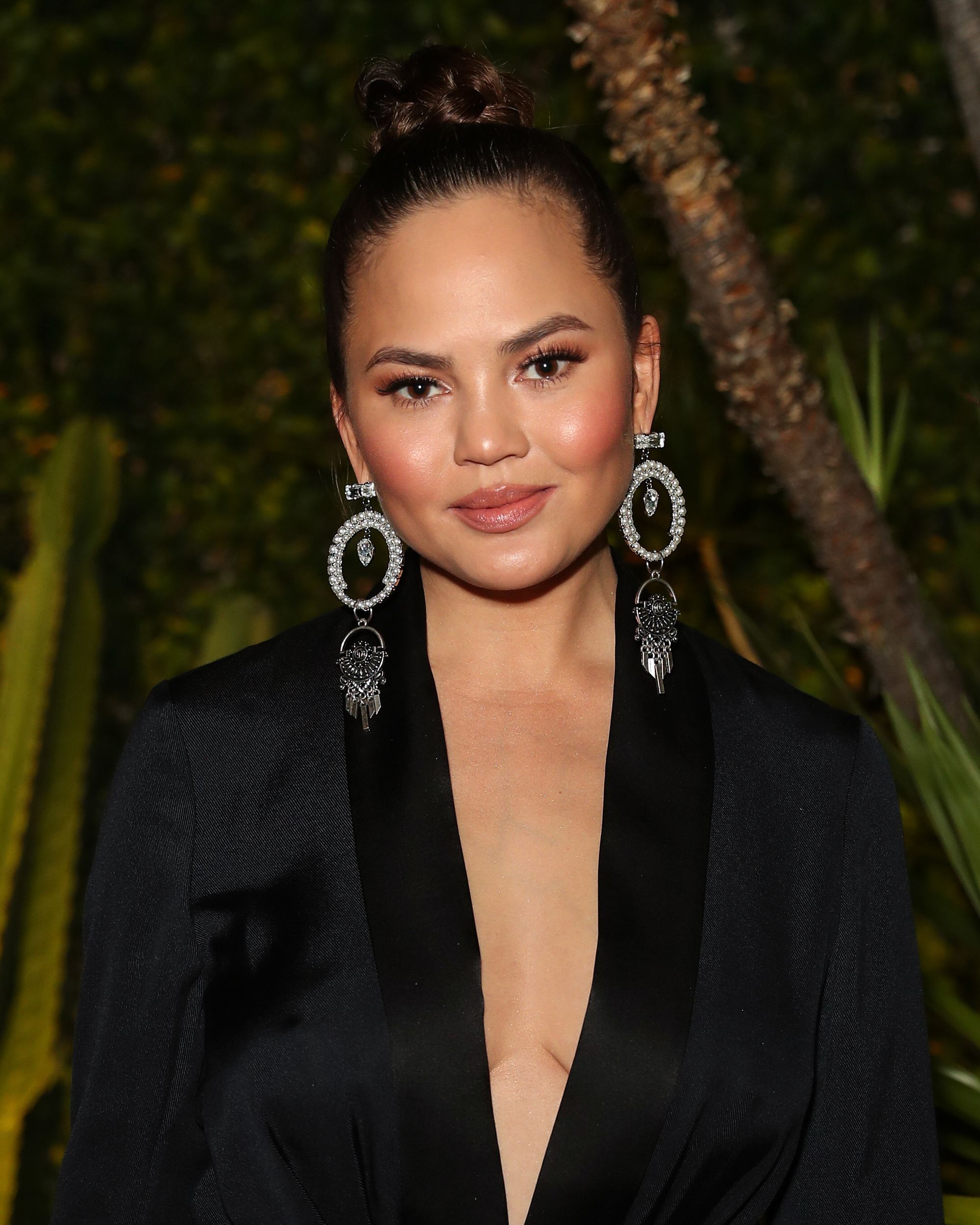 updo hairstyles for work: close up shot of chrissy teigen with braided top knot hairstyle on the red carpet, wearing all black