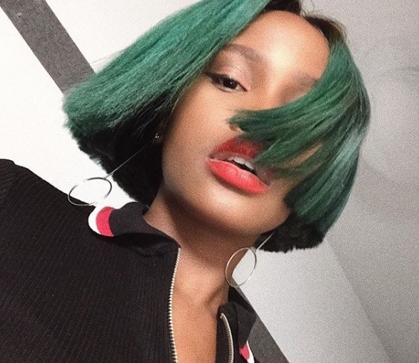 close up shot of woman with green short bob, wearing black top and posing with statement earrings