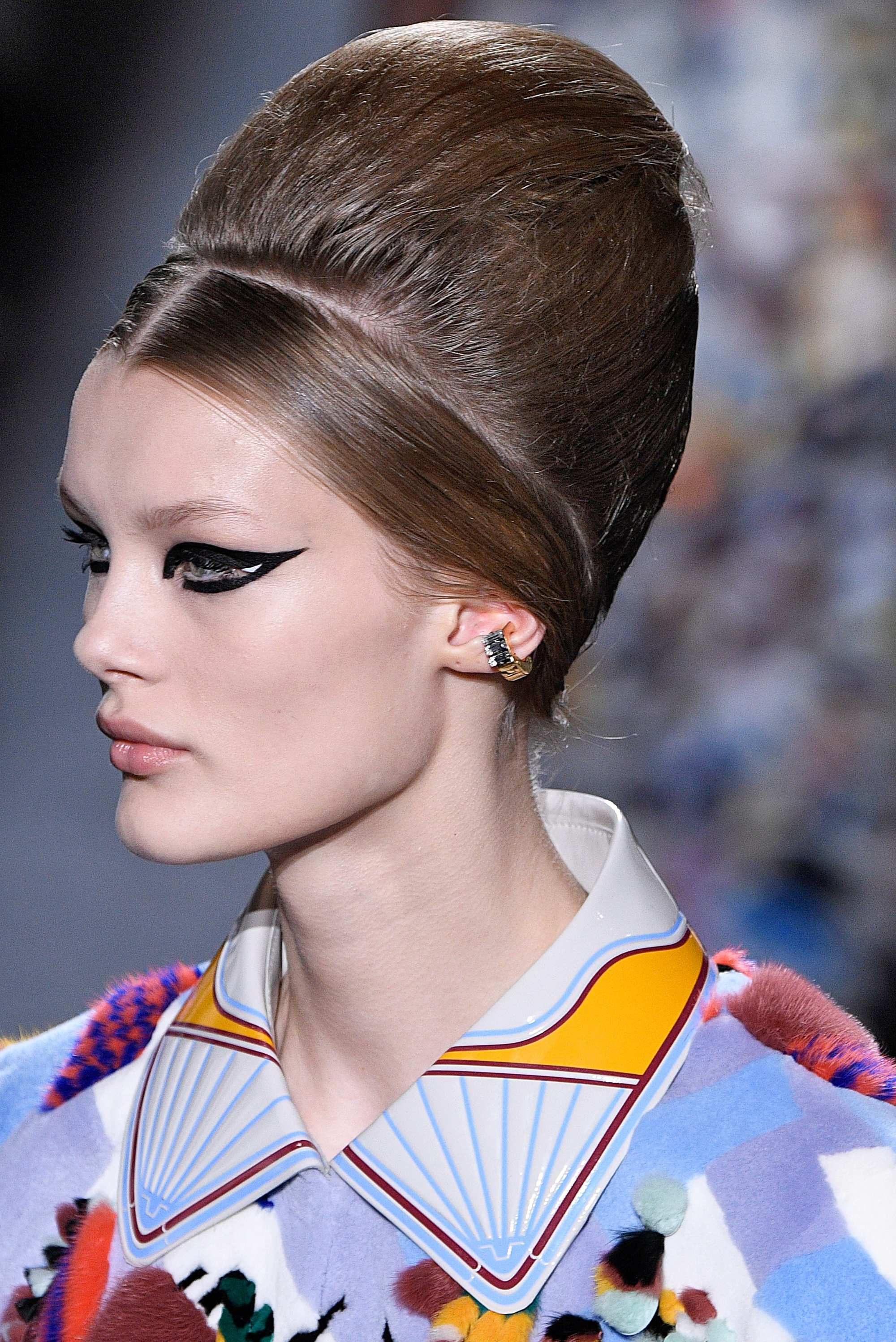 Paris Haute Couture Week fw18: close up shot of a woman with medium brown hair styled into a beehive updo, wearing cat eye liner and a printed top, on the fendi runway