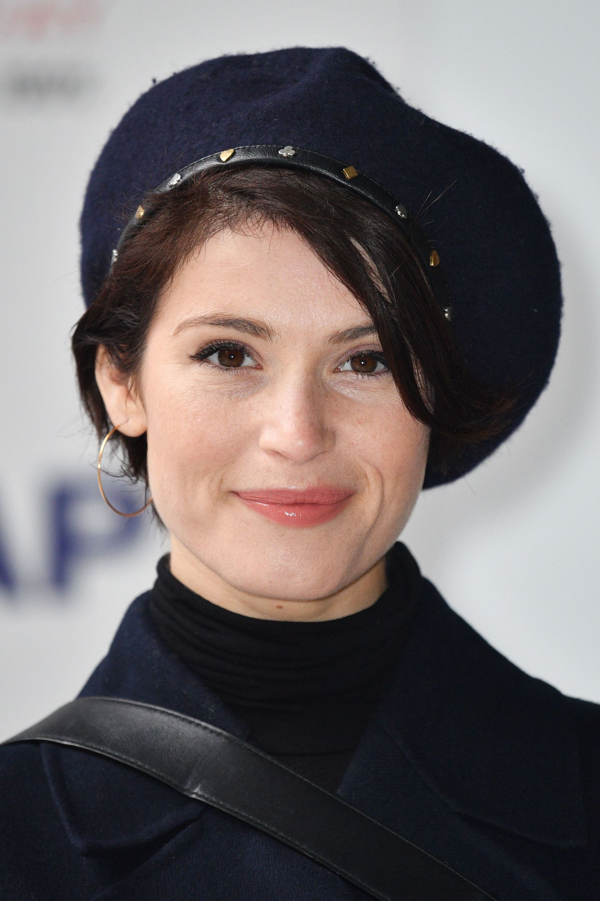 close up shot of gemma arterton with sleek pixie and beret hairstyle, posing and wearing all black on the red carpet