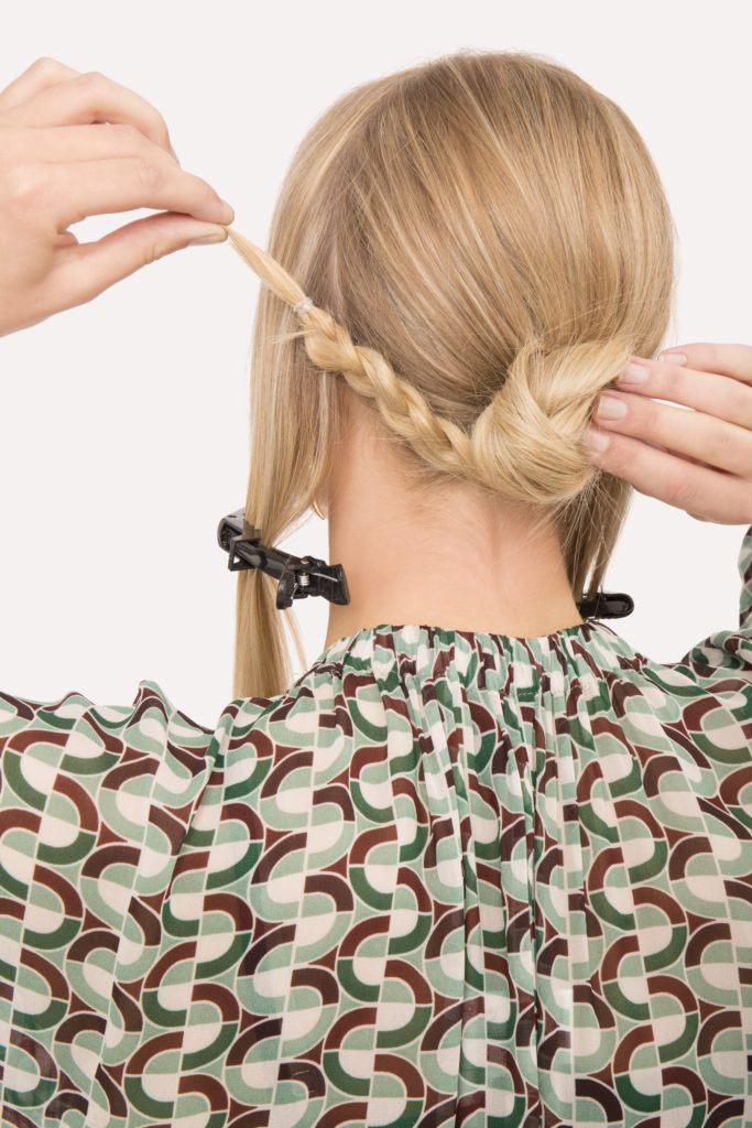 Braided updo blonde girl putting hair into a bun with back to camera