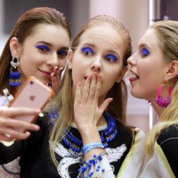 close up shot of three models backstage, posing and holding an iphone