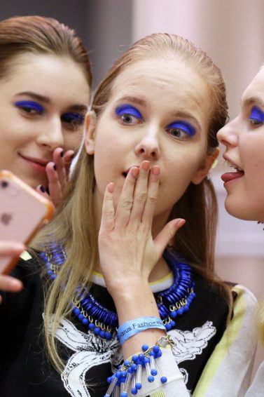 close up shot of three models backstage, posing and holding an iphone