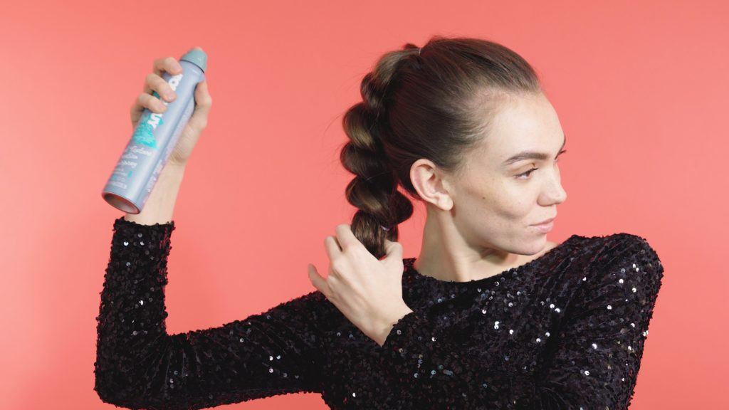 Brunette girl spraying her pull-through braid hairstyle with hairspray