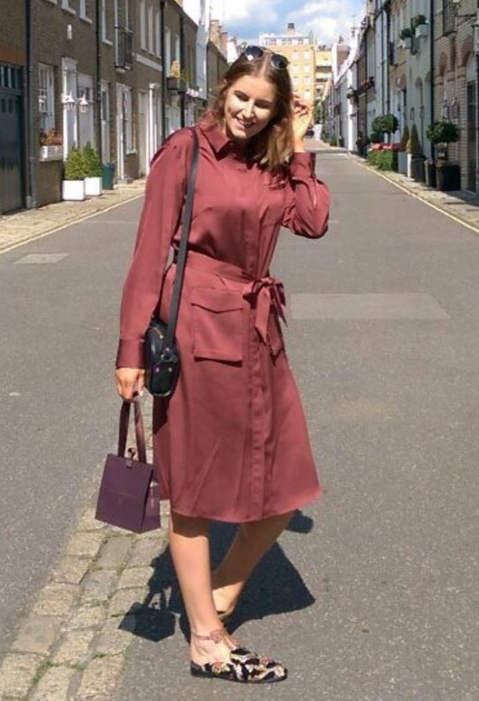 All Things Hair editor Leona with shoulder length long bob wavy brown hair, posing outside wearing a burgundy midi dress