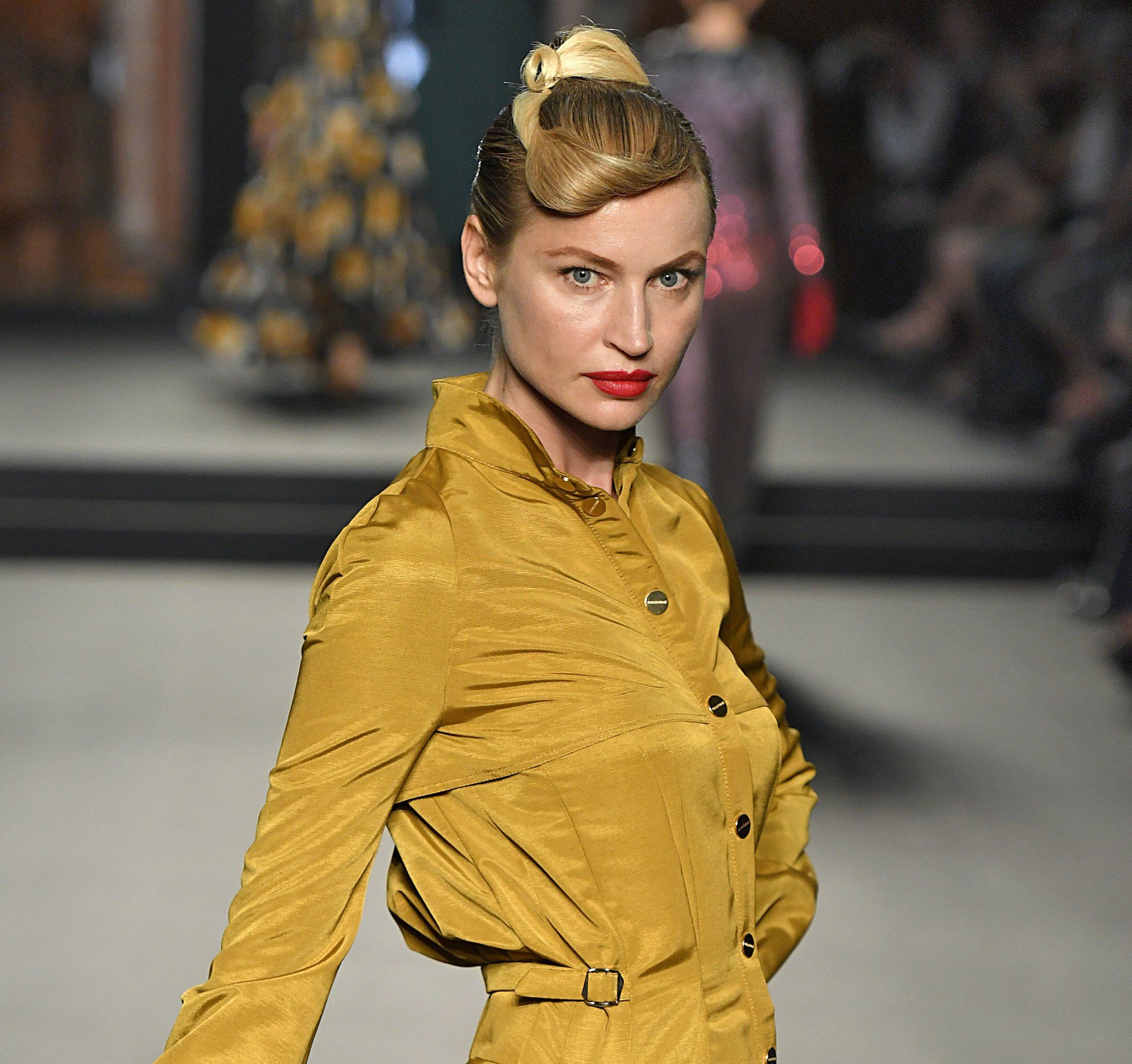 Paris Haute Couture Week fw18: close up shot of a woman on the runway with golden blonde hair styled into a retro twist updo, wearing mustard dress and posing