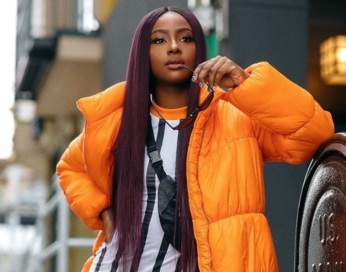 best hair colour for black women: close up shot of black woman with long purple hair, wearing orange jacket and stripped white shirt
