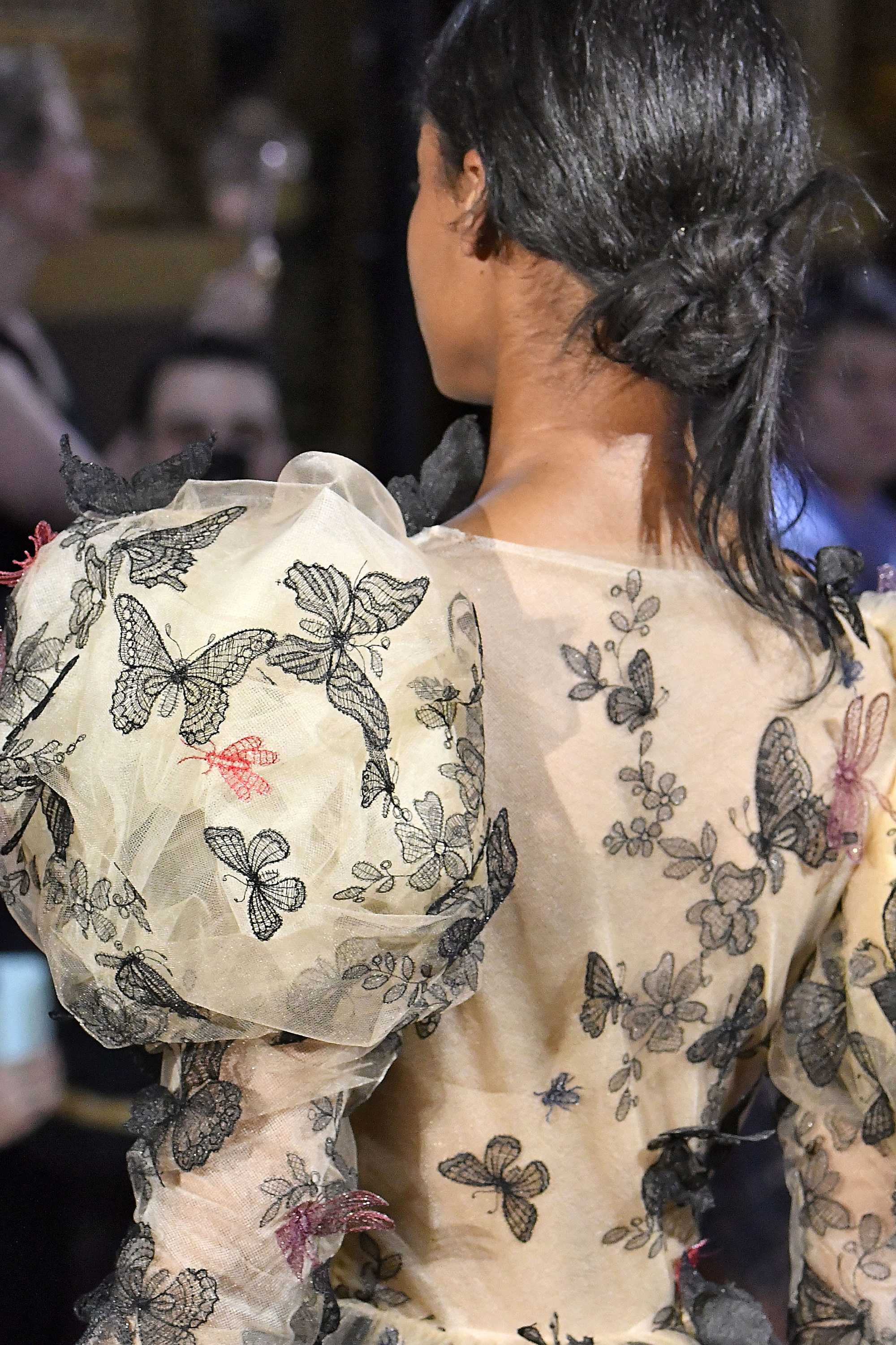 Paris Haute Couture Week fw18: close up shot of a model with dark brown hair styled into a low knotted bun, wearing a floral dress with puffy sleeves on the Schiaparelli runway