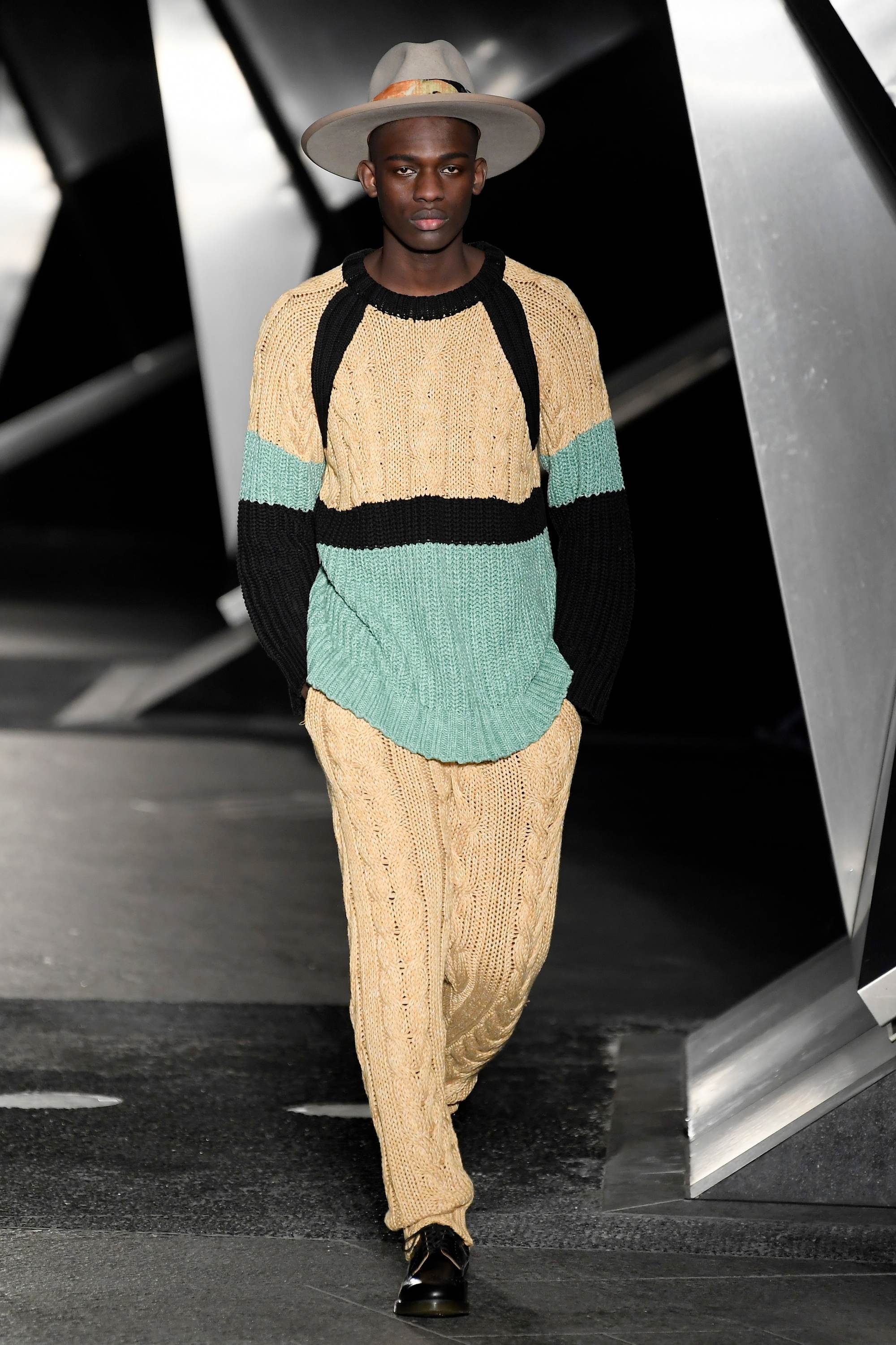 London Fashion Week Men's: Model on runway with fedora hat and yellow outfit.