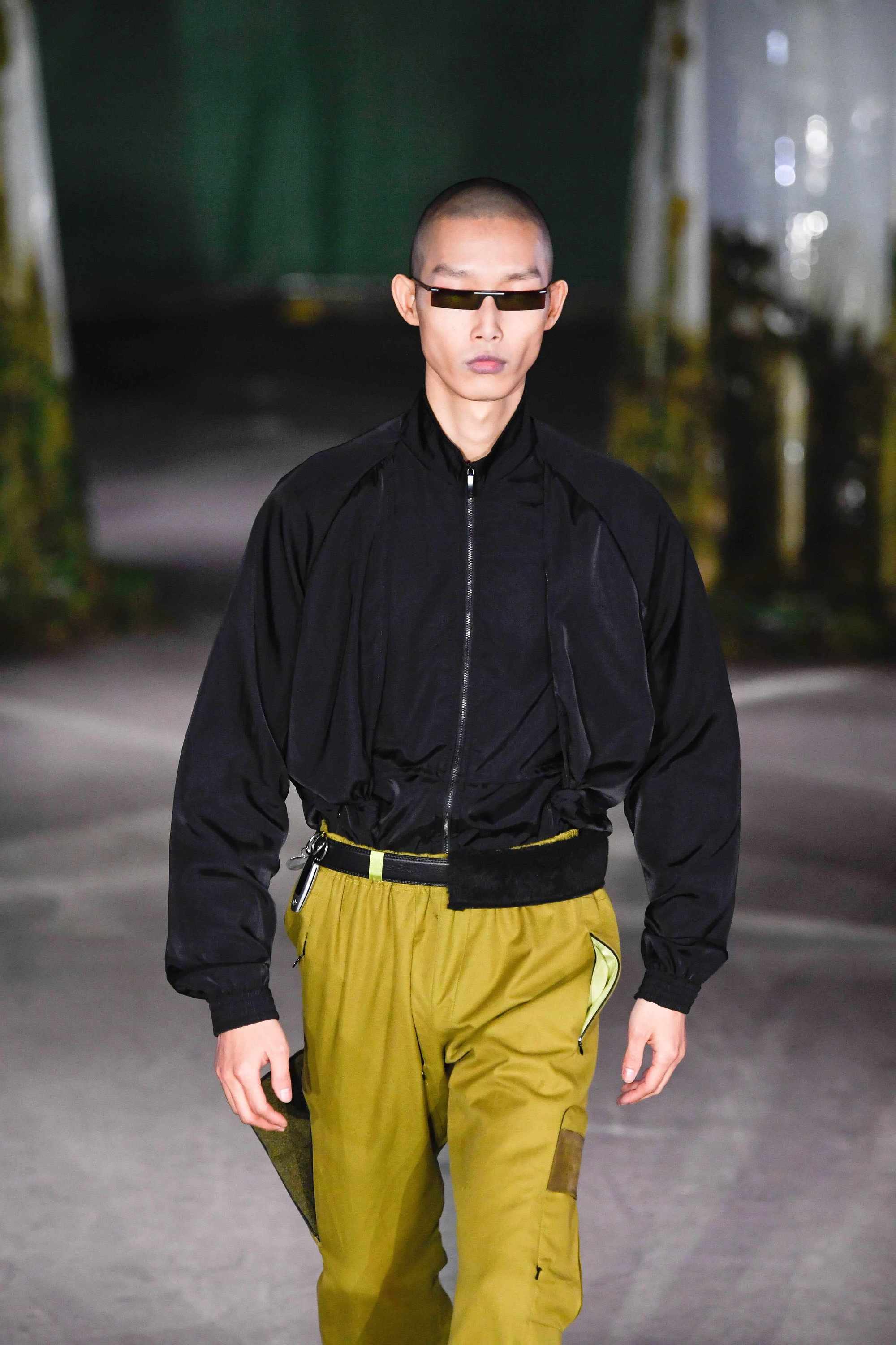 London Fashion Week Men's: Model on Cottweiler runway with shaved hair wearing micro black sunglasses.
