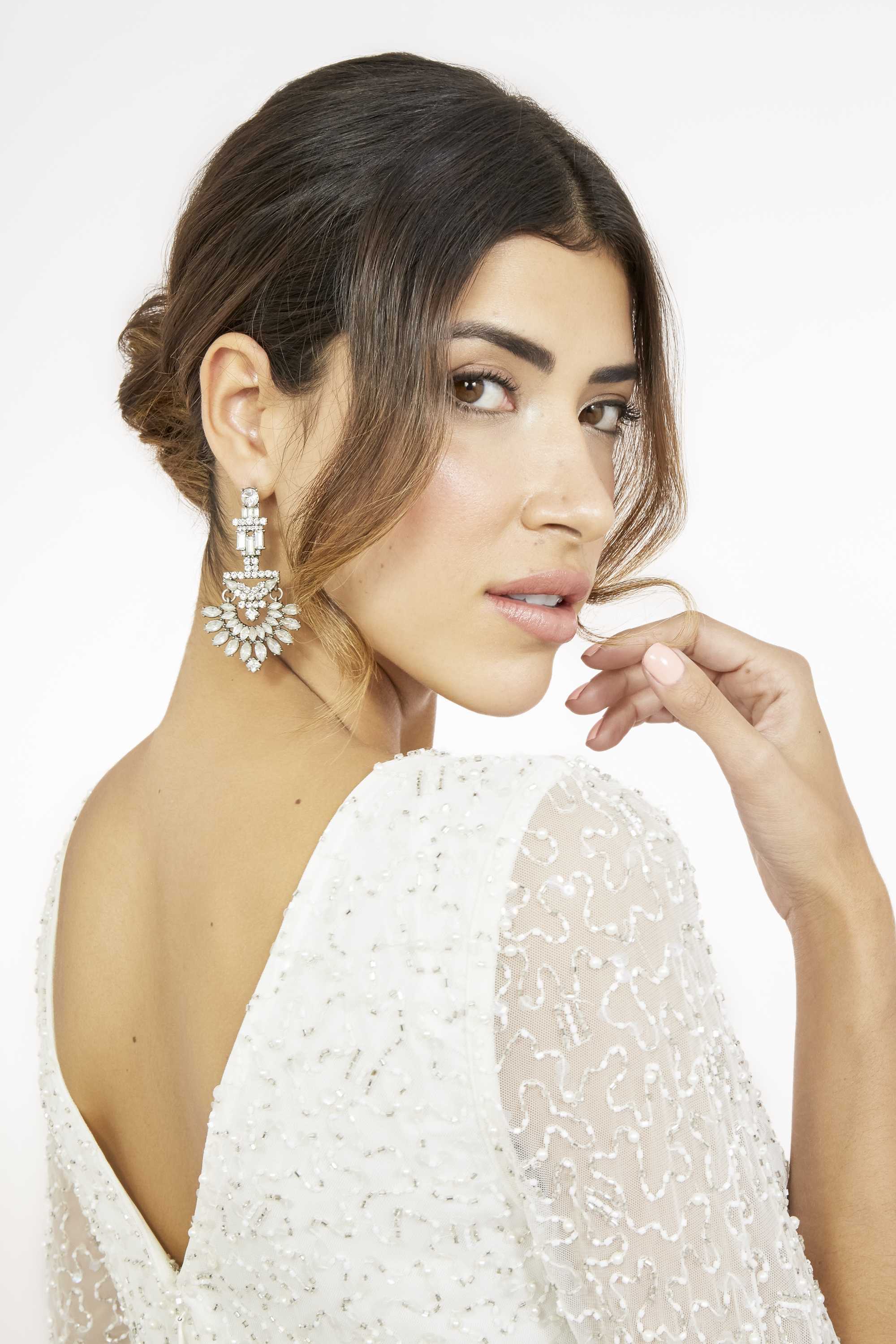 brunette model wearing a v back wedding dress with her hair in a low chignon with wavy loose face framing strands