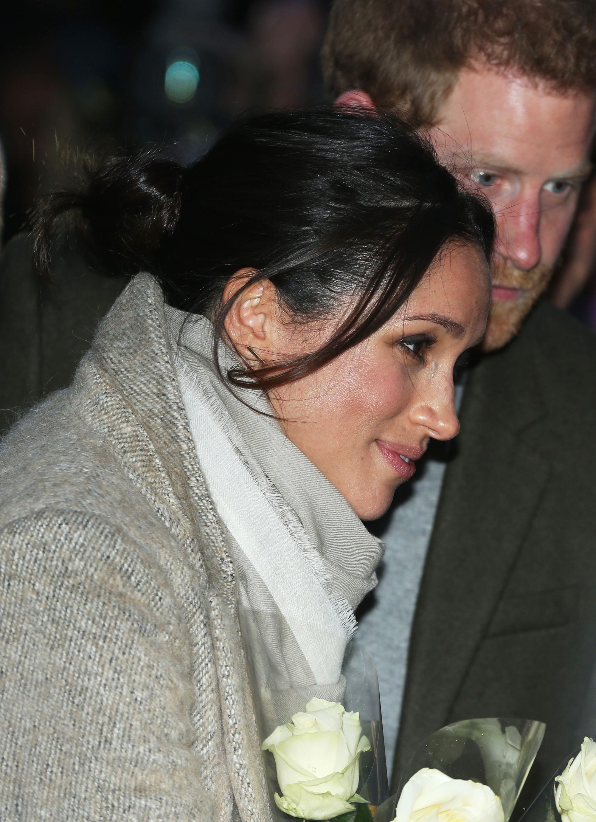 close up shot of meghan markle with low messy bun hairstyle, with loose tendrils at the front, standing next to prince harry on a recent outing