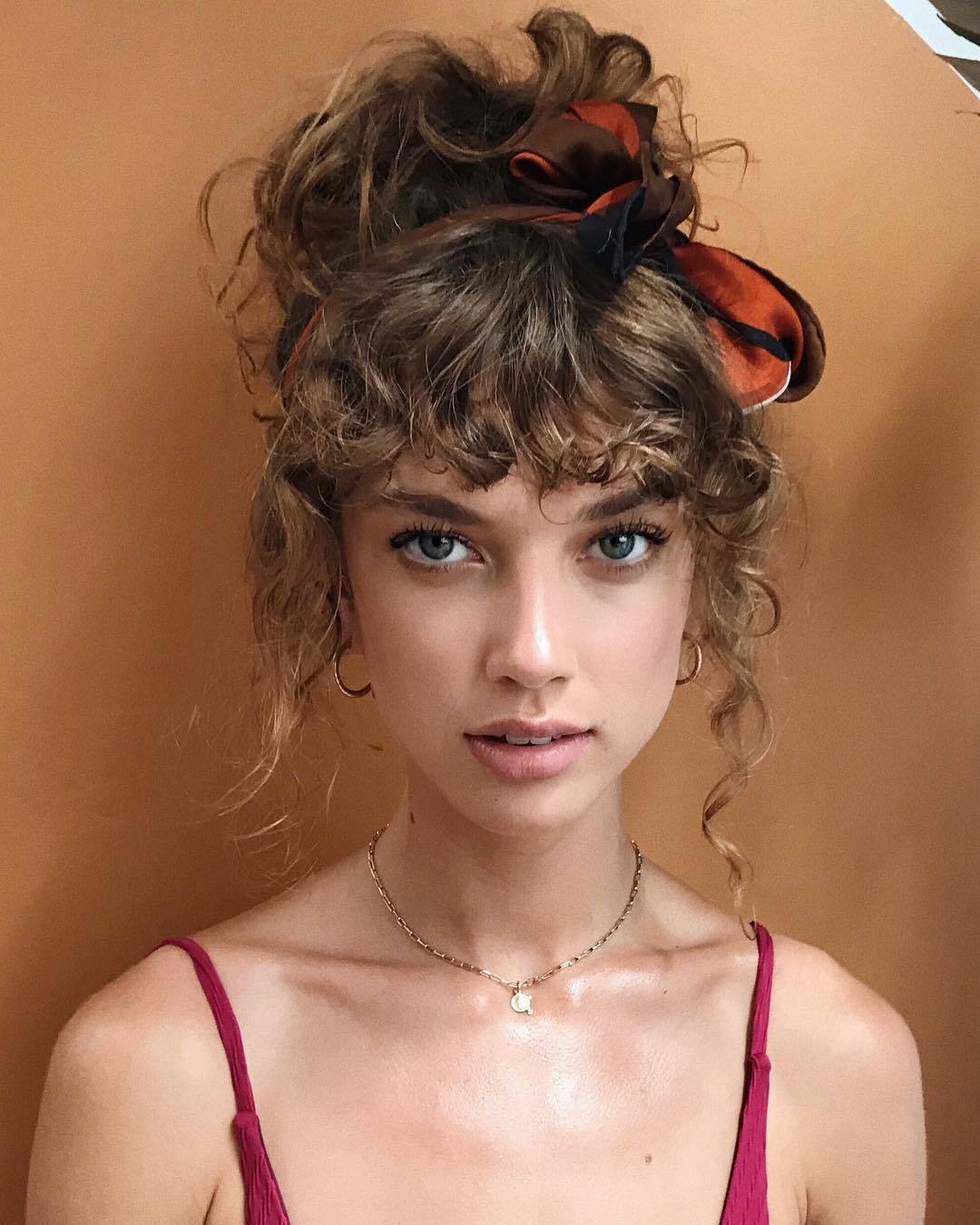 Permed hair care girl with curly brown hair in updo and scarf in hair looking at camera