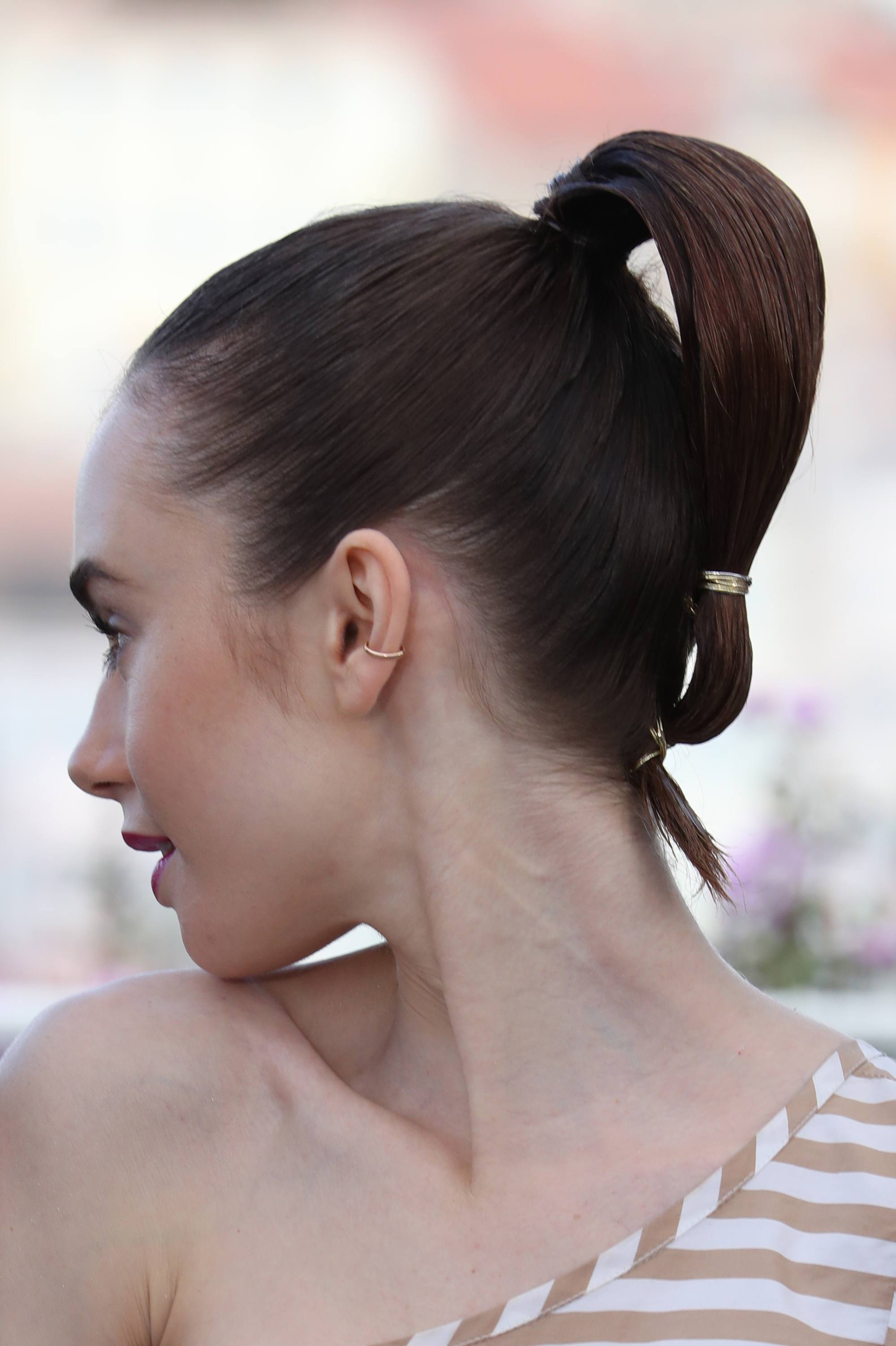 straight short hairstyles: close up shot of lily collins with sleek low looped ponytail, wearing all white on the red carpet and posing