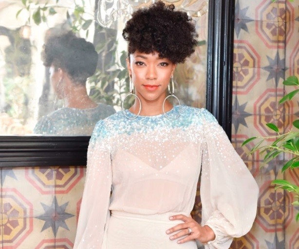 close up shot of Sonequa Martin-Green with pineapple hairstyle, wearing white see through dress and posing at an event