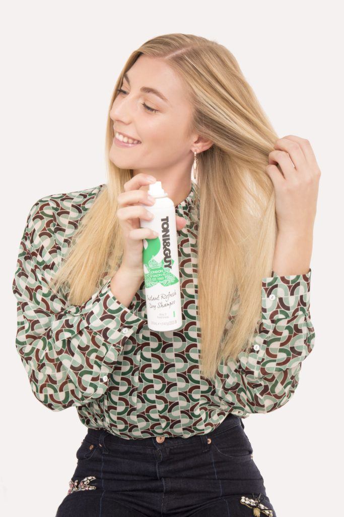 Braided bun tutorial blonde girl spraying dry shampoo on hair