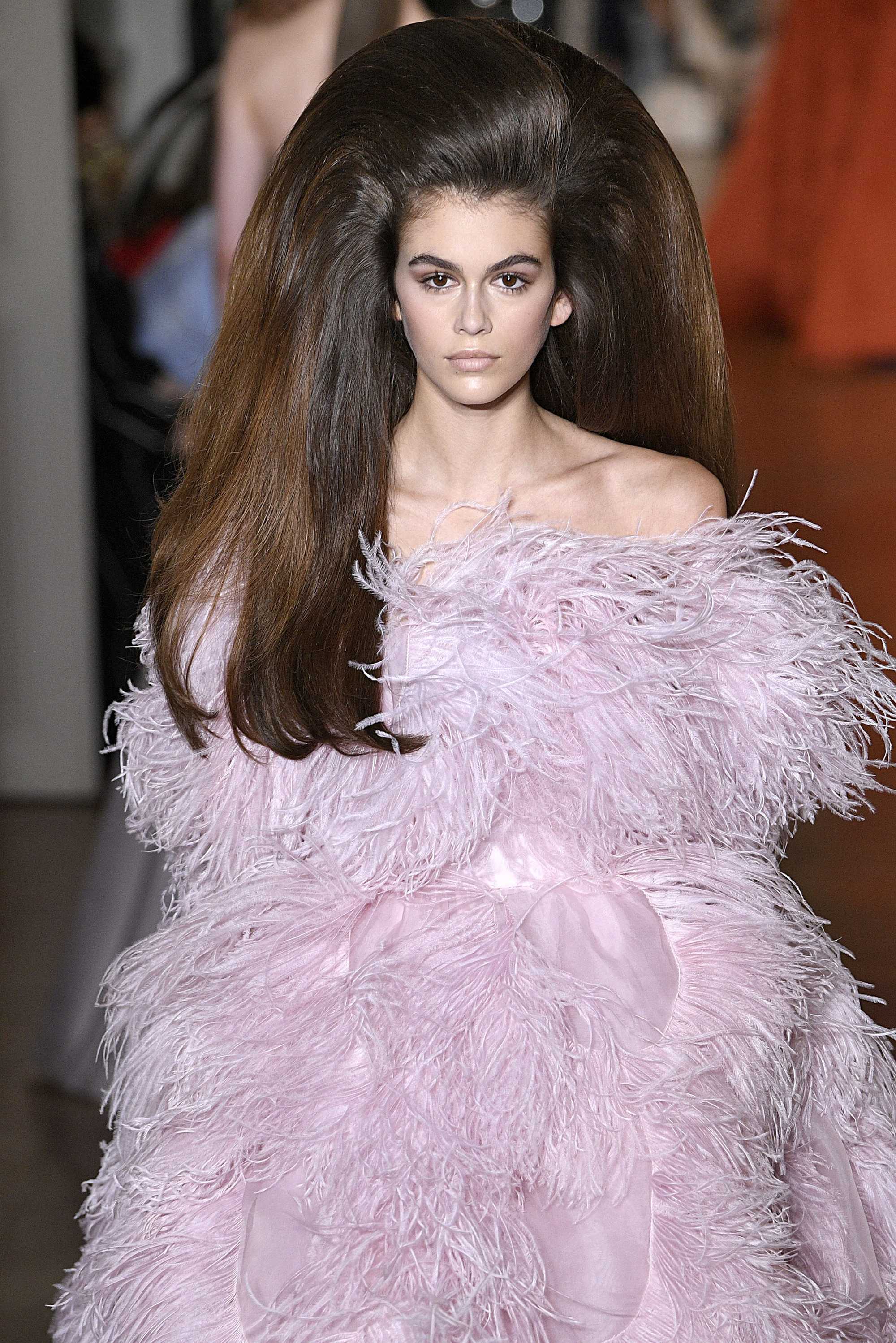 Paris Haute Couture Week fw18: close up shot of a model on the runway with chocolate brown hair styled into a glamorous bouffant, wearing a feathery purple dress and walking down the Valentino runway