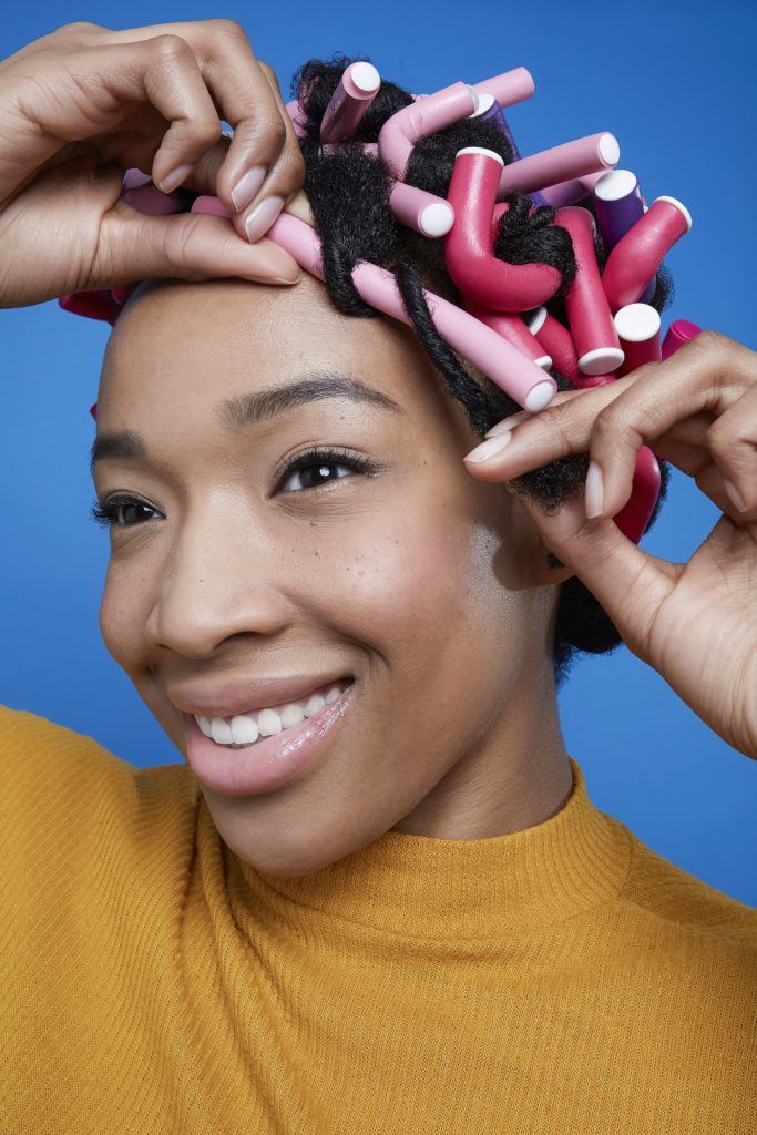 Black girl smiling and unraveling flexi rods from hair