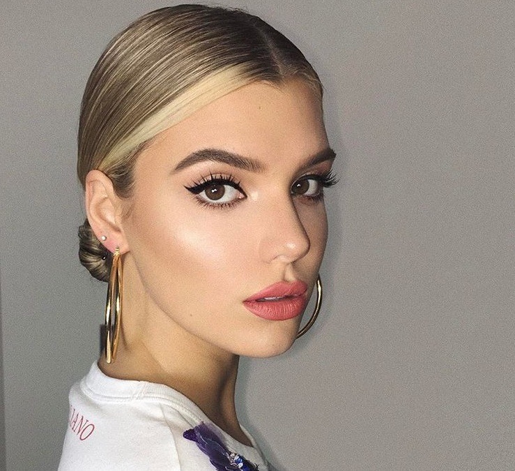 Night out hairstyles: Woman with short golden blonde styled into a low sleek bun, wearing hoop earrings in a bedroom setting