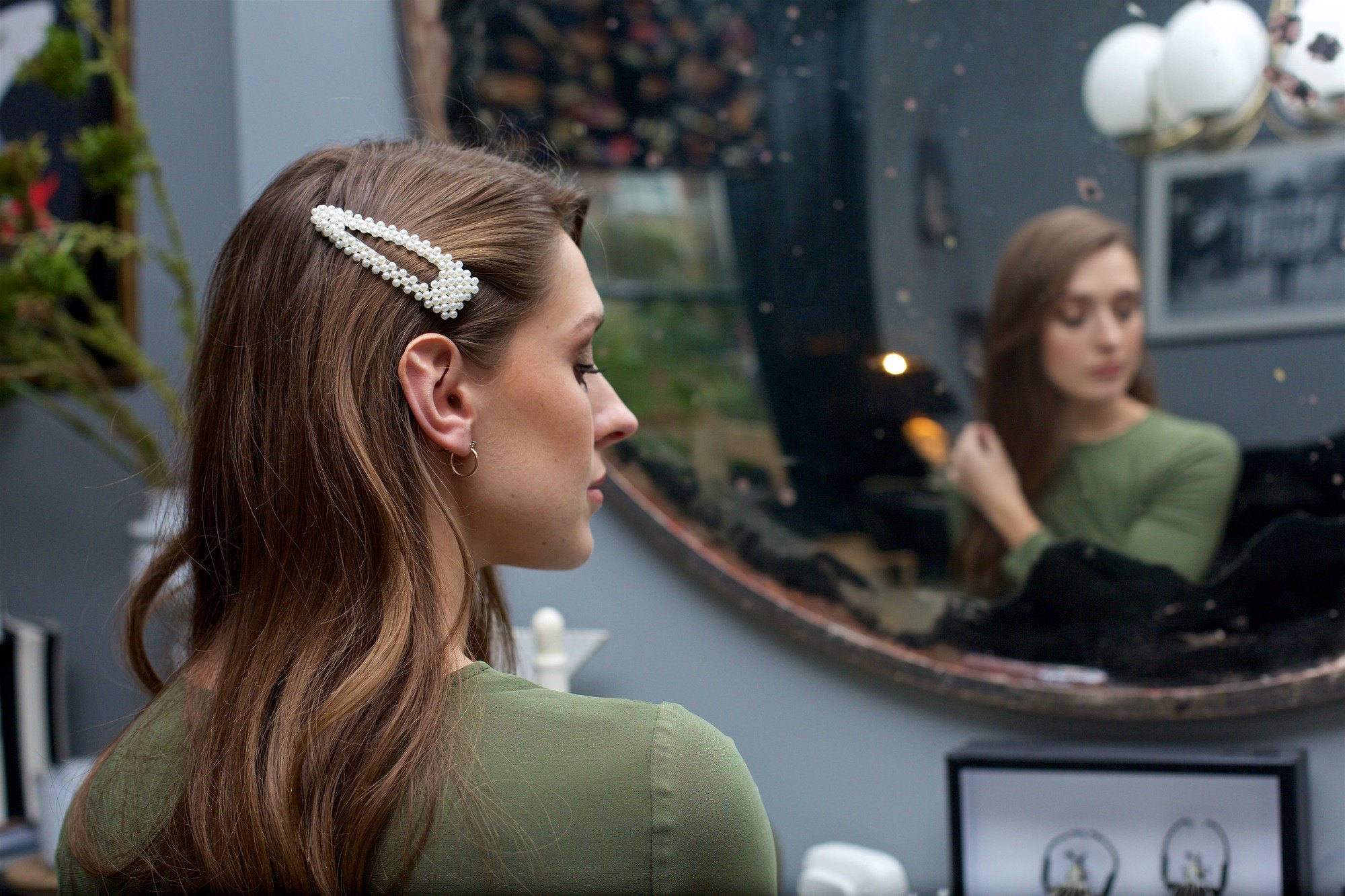 Spring haircuts: Woman with long wavy brunette highlighted hair with an oversized pearl hair clip, doing her hair in the mirror