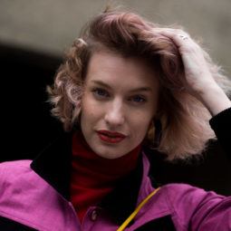 best hair mousse guide: close up street style shot of woman with pastel pink wavy bob, wearing pink jacket and red scarf