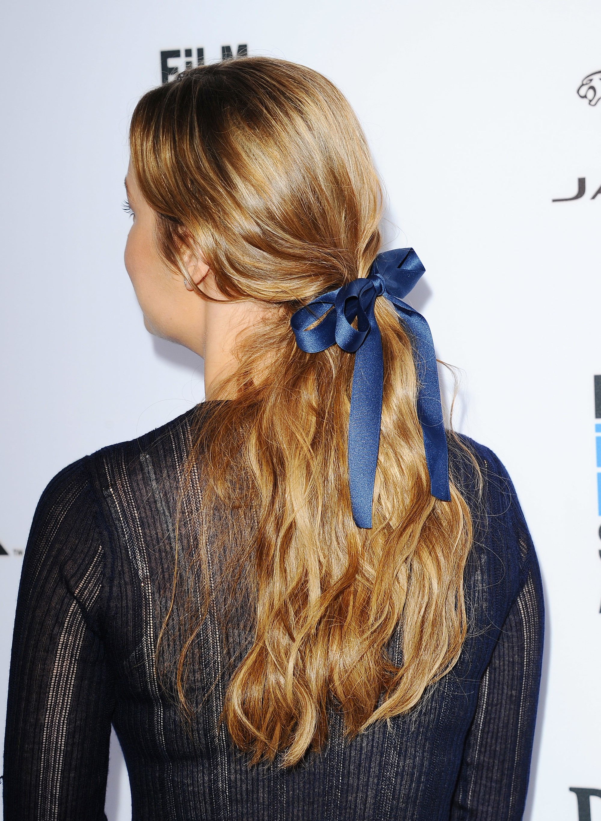 cute hairstyles for long hair: close up shot of brie larson with low messy ponytail with bow on it