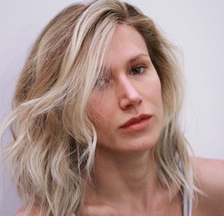 close up shot of woman with wispy layers and bangs, wearing white spaghetti top and posing for photo