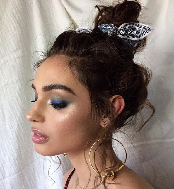 Night out hairstyles: Woman with chocolate brown wispy hair styled into a messy topknot bun, wearing hoop earrings and posing outside