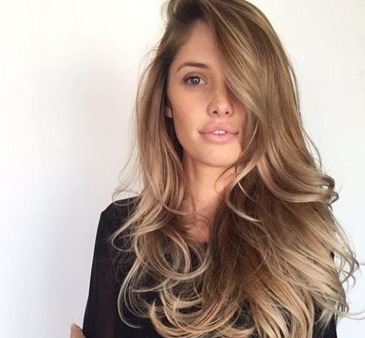 Night out hairstyles: Woman with blown out ash brown long hair swept to the side, wearing a black top and posing in a studio