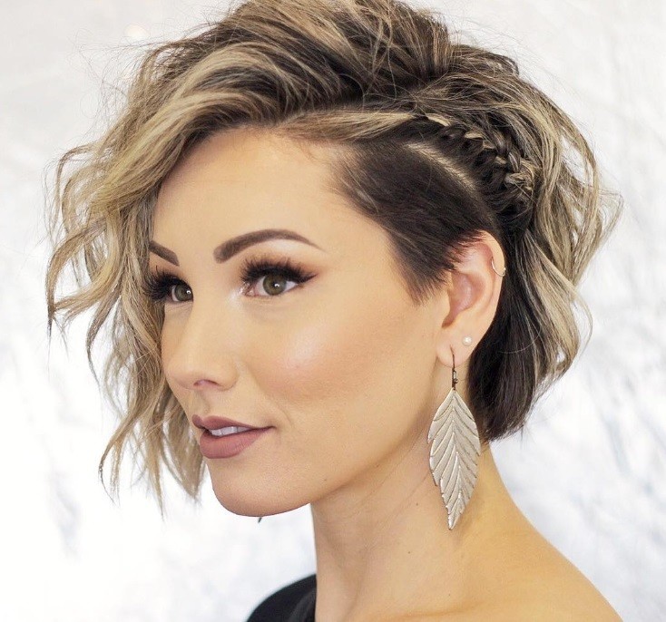 Short night out hairstyles: Woman with short hair with undercut styled into beachy waves, with a side braid in it, posing in a studio setting