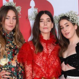 close up shot of the haim sisters with beachy waves, wearing baby's breath in their hair and posing on the brit awards 2018 red carpet