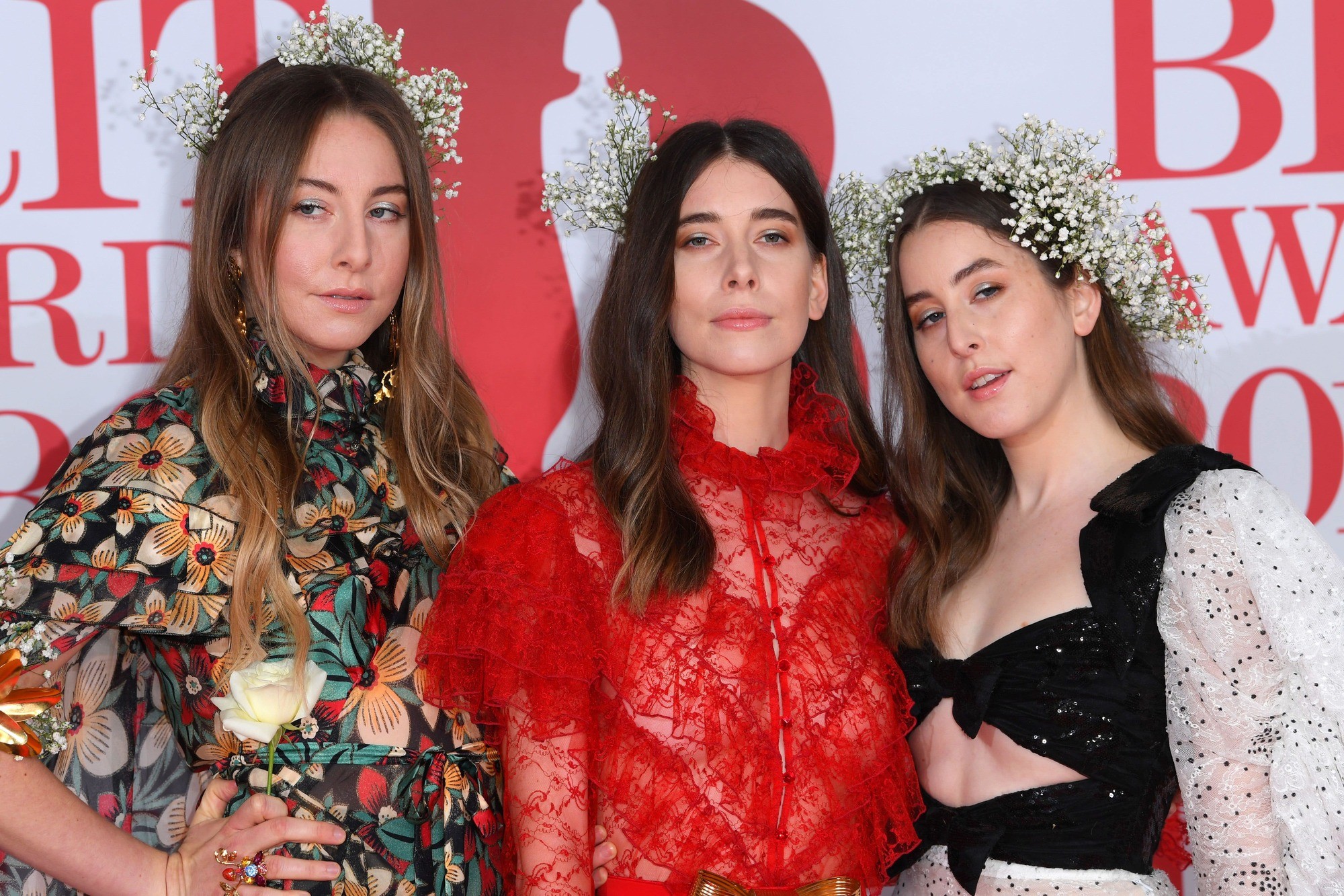 close up shot of the haim sisters with beachy waves, wearing baby's breath in their hair and posing on the brit awards 2018 red carpet