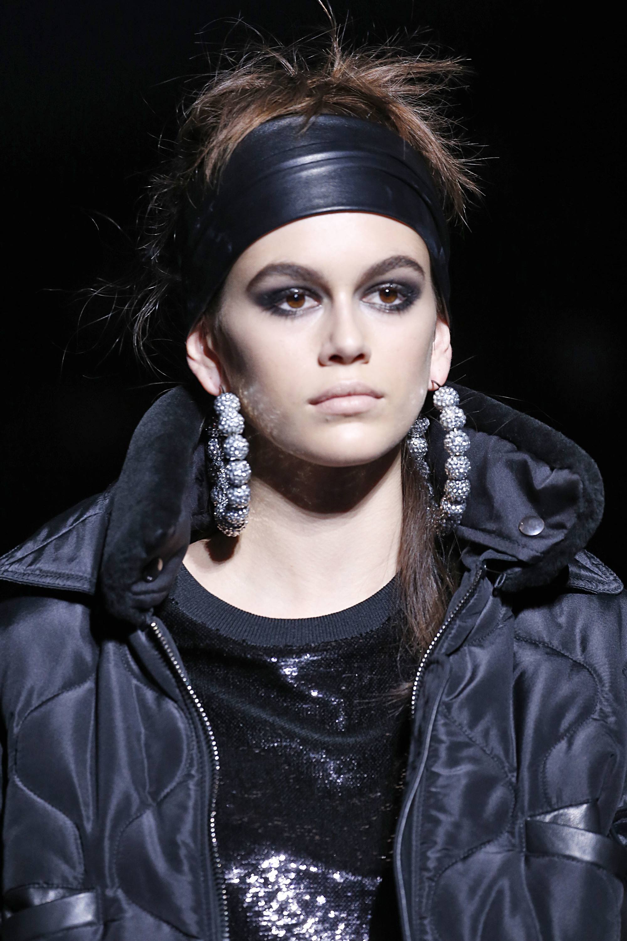 kaia gerber on tom ford runway with brown hair in updo with large black leather headband and large hoop earrings