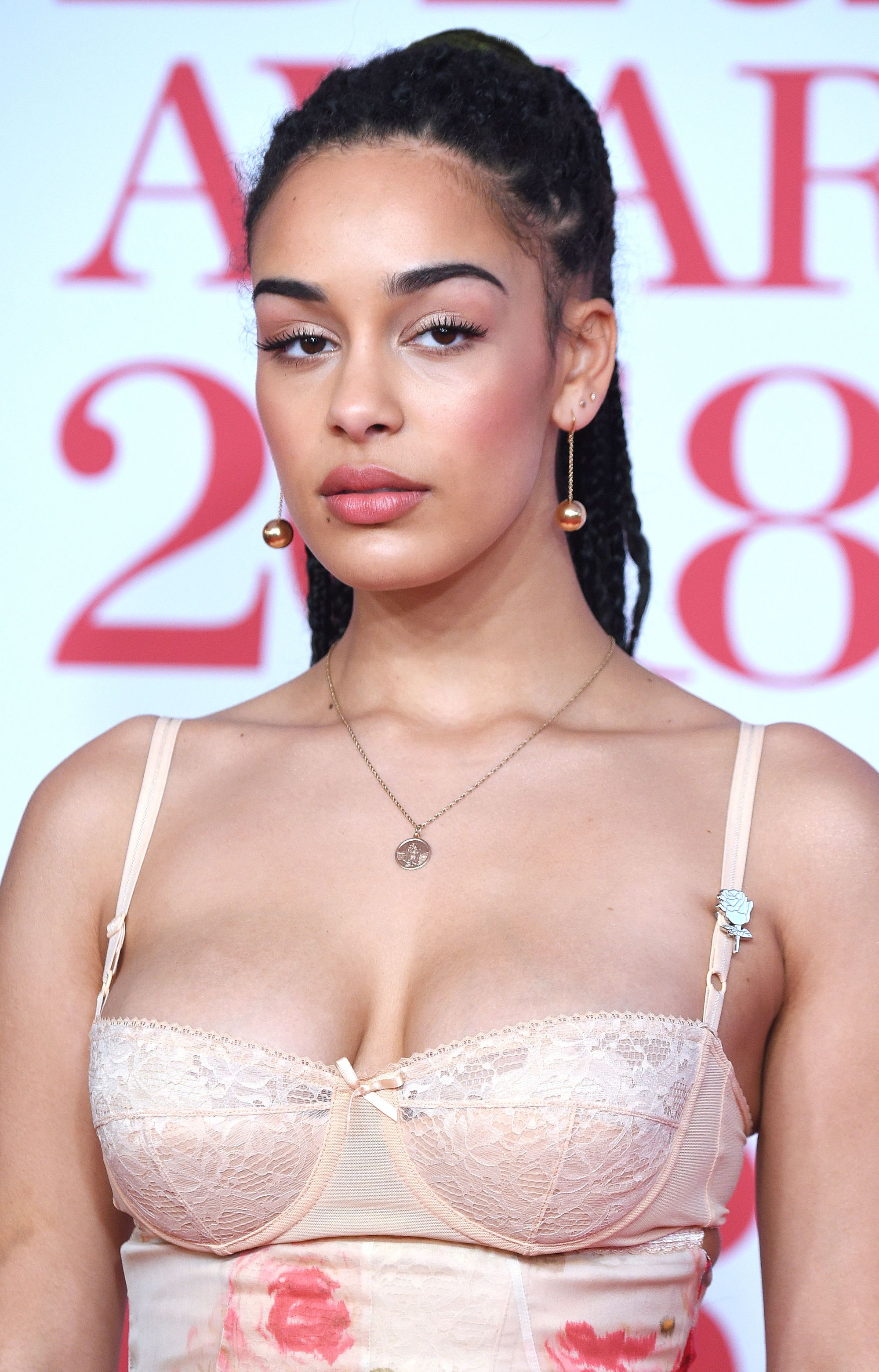 close up shot of jorja smith with half up half down box braids, wearing pink floral dress with drop rose gold earrings and posing on the brit awards 2018 red carpet