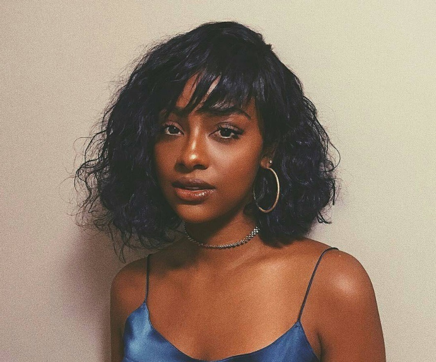 short weave hairstyles: close up shot of woman with short wavy weave with bangs, wearing hoop earrings and posing for a photo