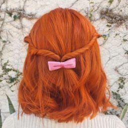 short red hairstyles: close up shot of woman with ginger hair styled into a half up half down twisted style with bow
