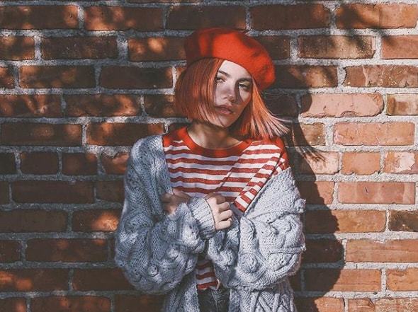 close up shot of woman with short ginger and peach red hair, wearing striped top, red beret and a long cardigan