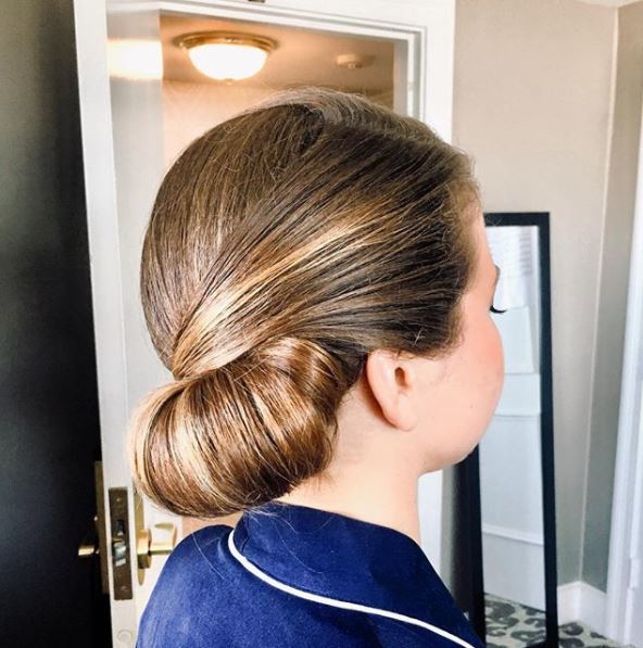 side view of woman with brunette hair in smooth and sleek side tuck bun hairstyle wearing navy top