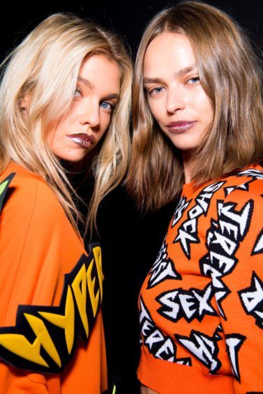 Thickening shampoo products guide: Two models backstage with short and medium wavy, volumised hair wearing slogan jumpers backstage
