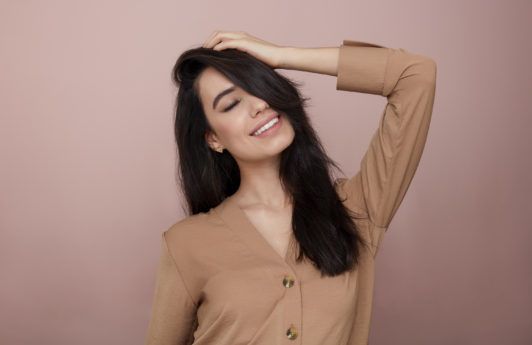 What is a hair mask: Woman touching her long dark brown hair, wearing brown nude jumper in the All Things Hair UK Studio