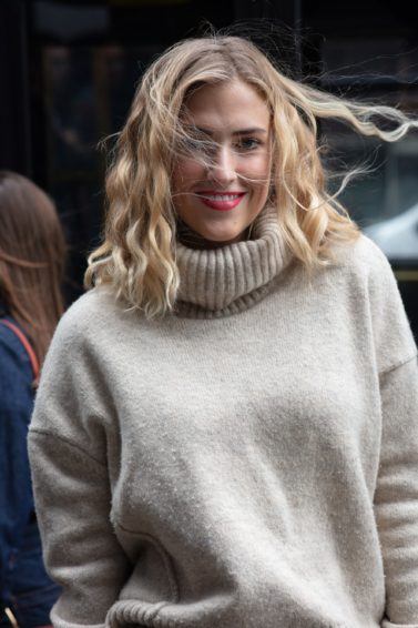 Hair hacks for winter: Shot of a woman with beige turtleneck, with medium golden blonde curly hair posing for street style picture