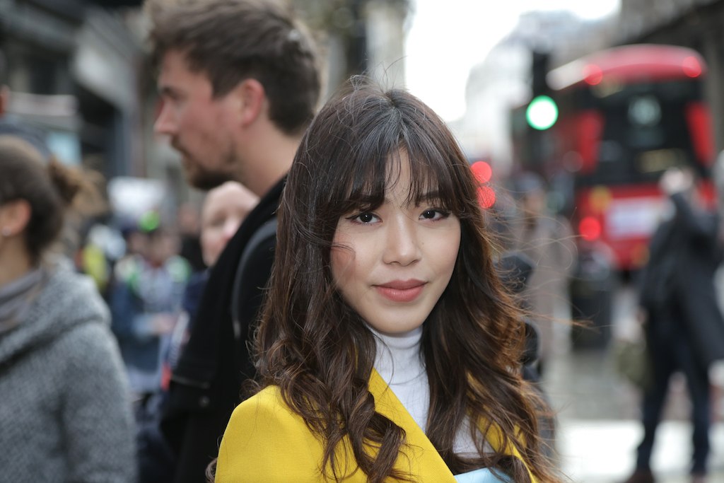Spring haircuts: Asian street styler with long curly hair and curtain bangs, wearing a yellow blazer