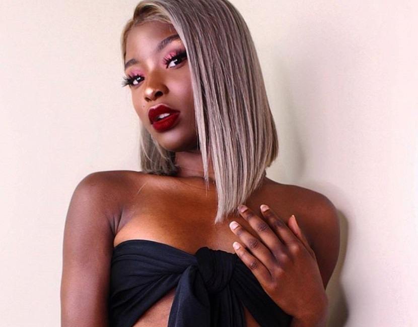 short weave hairstyles: close up shot of woman with blunt cut asymmetric bob hairstyle that is silver, posing and wearing black crop top