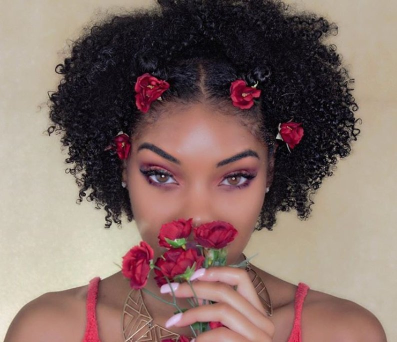 close up shot of women with natural hair with flowers in it, holding small red flowers and posing