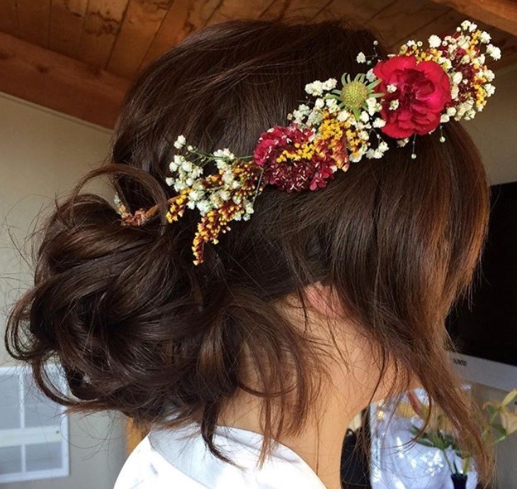textured hairstyles: close up shot of woman with messy bun hairstyle, wearing floral crown and white dress