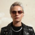 british model cara delevingne with a platinum blonde pixie cut wearing a black top and black leather jacket
