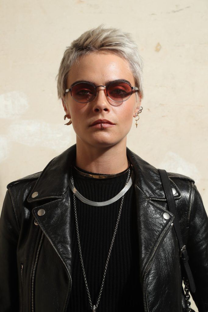 british model cara delevingne with a platinum blonde pixie cut wearing a black top and black leather jacket