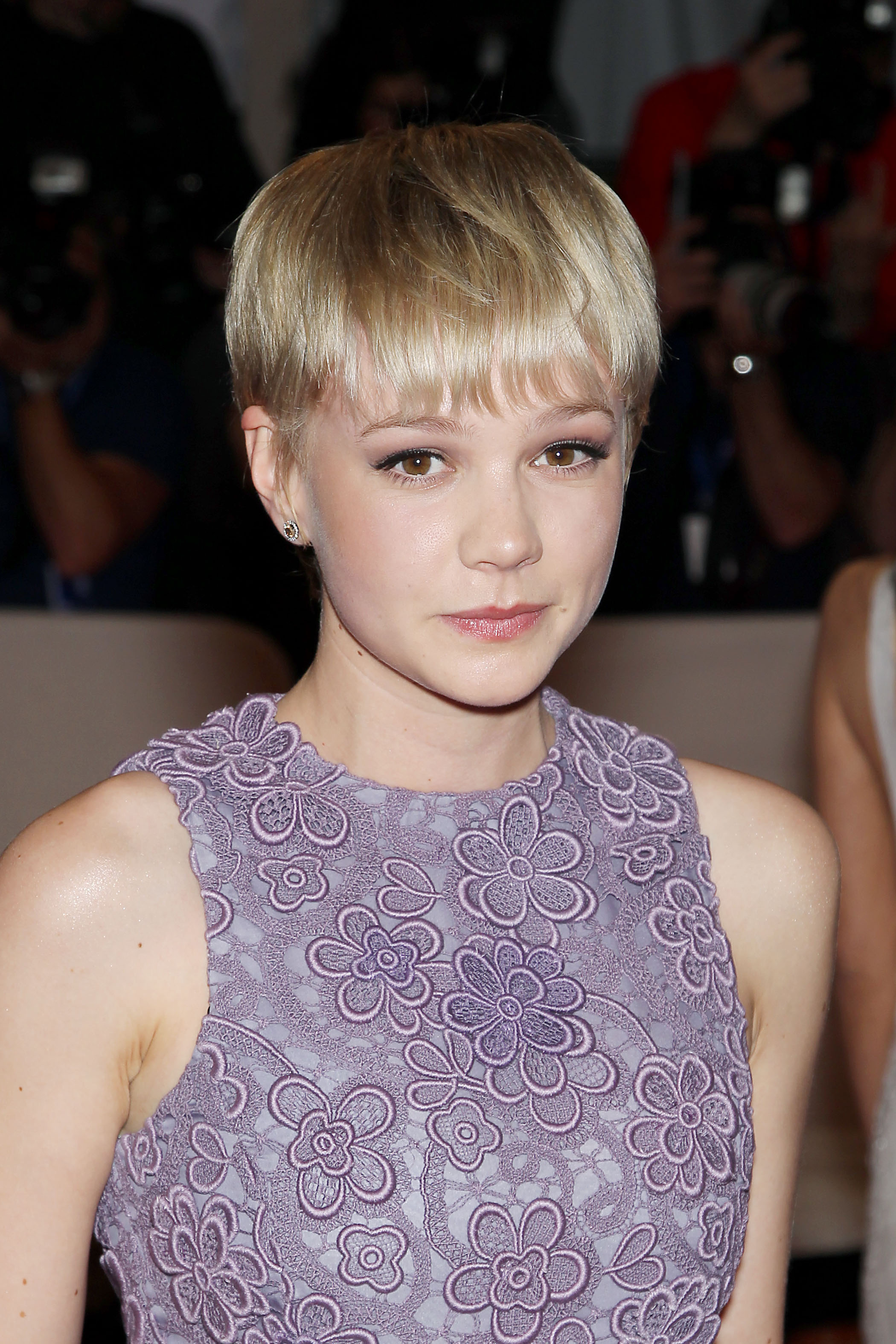 Pixie cut with bangs: Carey Mulligan with a blonde bowl cut pixie, wearing a sleeveless purple lace dress
