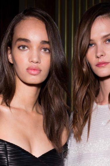 Frizzy hair products guide: Two models with brown hair that has been styled into smooth, polished waves, wearing Balmain clothing backstage