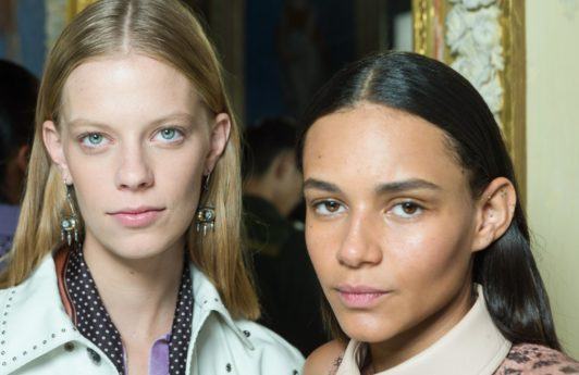 Two models backstage at the Bottega Veneta show with smooth, straight hair staring into the camera